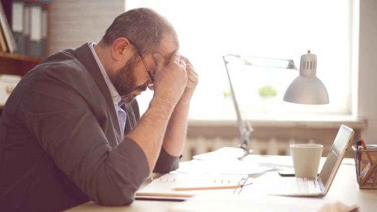 Man sits at his desk, head in hands looking upset