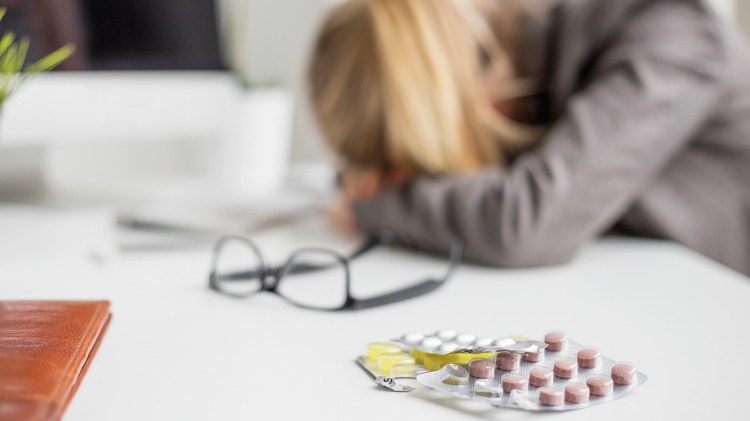 Woman's head down on her desk with medication sitting in the foreground